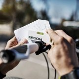 Zwei Hände halten eine kleine Wasserwaage und eine Karte mit Grafiken darauf an einen Fahrradlenker.