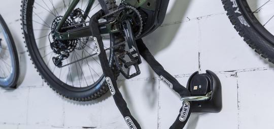 Ein an einer Wand hängendes Fahrrad ist mit einem Fahrradschloss an einer darunter angebrachten, festen Verankerung gesichert.