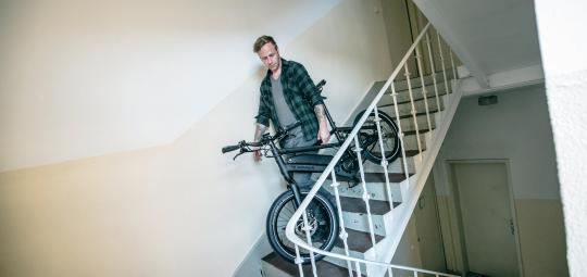 Ein Mann trägt ein E-Bike die Treppe in einem Wohnhaus hinunter.