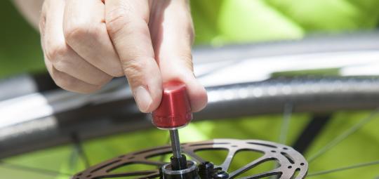 Eine Person hält ein Laufrad an der Nabe vor sich und greift die Mutter eines Schnellspanners mit zwei Fingern.