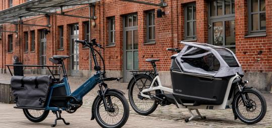 Zwei Lastenräder vor einem Gebäude mit Ziegelfassade.