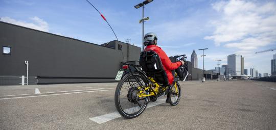 Eine Person fährt auf einem Liegerad in Richtung einer Großstadt-Skyline.