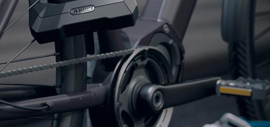 Ein Fahrrad ist mit dem Bügelschloss Granit Super Extreme 2500 von ABUS an einem Fahrradständer angeschlossen. Im Vordergrund liegt ein Trennschleifer auf einer Bank.