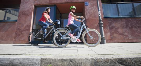 Ein Kind und eine Frau fahren auf einem Gehweg Rad.