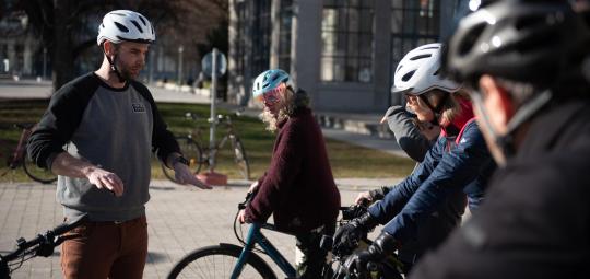 Ein Mann steht vor einer Gruppe Radfahrer:innen und erklärt etwas mit den Händen.