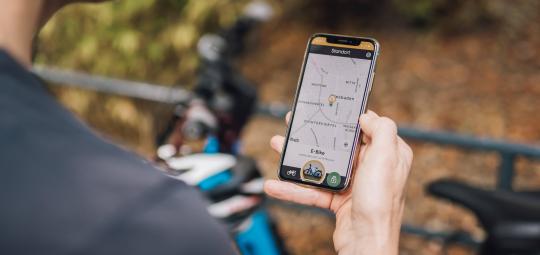 Blick über die Schulter einer Person, die ein Smartphone mit einer Karten-App vor sich hält.