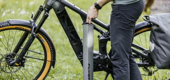 Eine Person steht neben einem E-Bike und hält den länglichen Akku in der Hand, der im Rahmen montiert wird.