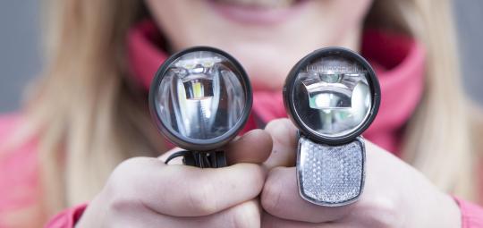 Eine Frau hält zwei Fahrradscheinwerfer vor sich.