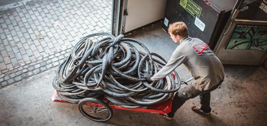 Ein Mann schiebt einen Fahrradanhänger mit alten Fahrradreifen aus einem Tor heraus.