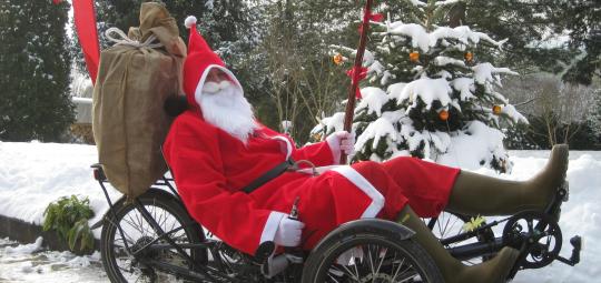 Eine als Weihnachtsmann verkleidete Person auf einem Liegedreirad.