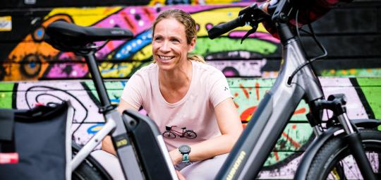 Eine Frau sitzt lächelnd hinter einem abgestellten E-Bike.