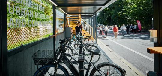 In einem einseitig offenen Metallcontainer stehen mehrere Fahrräder an Haltevorrichtungen.