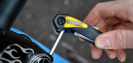 Ein Faltwerkzeug mit Innensechskantschlüssel in der Hand einer Person, die damit an dem Vorbau eines Fahrrades schraubt.