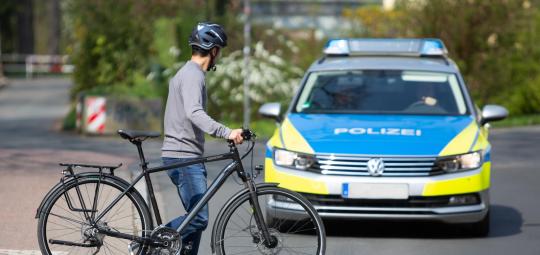 Eine Person schiebt ein Fahrrad über einen Fußgängerüberweg und schaut zu einem Polizeiauto auf der Fahrbahn.