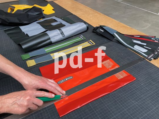 Eine Person schneidet mit einem Arbeitsmesser und einem Metalllineal Materialien einer Fahrradtasche.