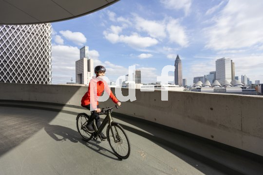 Eine Frau fährt mit einem E-Bike vor der Skyline von Frankfurt entlang.