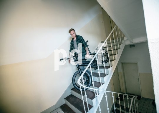 Ein Mann trägt ein E-Bike die Treppe in einem Wohnhaus hinunter.