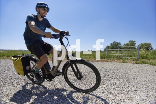 Ein Radfahrer fährt mit einem E-Bike über einen Schotterweg auf dem Land.