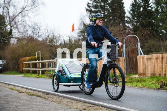 In Kinderanhänger lassen sich bis zu zwei Kinder mitnehmen. Mann fährt mit E-Bike und Anhänger