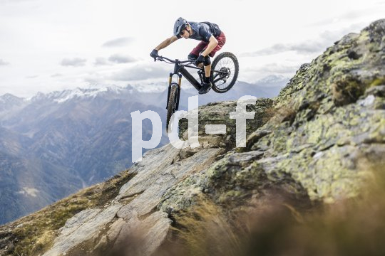 E-Mountainbikes erfreuen sich einer wachsenden Beliebtheit sowohl bei Profis als auch bei Einsteiger:innen. Mann springt mit E-Mountainbike über ein Hindernis in den Bergen.