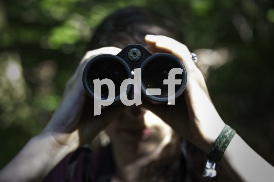 Eine Person schaut durch ein Fernglas in Richtung des Betrachtenden.
