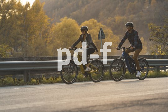 Paar fährt auf E-Bikes auf der Landstraße.