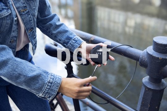 Eine Person schließt ein Fahrrad mit einem dünnen Stahlseil an einem Geländer an.
