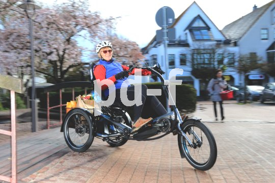 Eine Person auf einem Dreirad mit Tretkurbel, Motorunterstützung und Gepäck zwischen den beiden Hinterrädern.