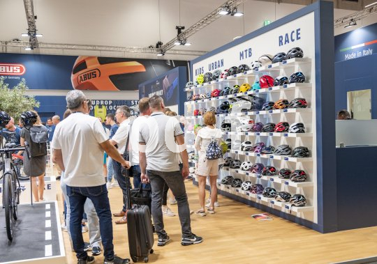 Mehrere Personen stehen vor einer Wand, an der viele Fahrradhelme präsentiert sind.