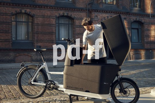 So lässt sich fast alles per Rad transportieren, und das auch noch regensicher. Ein Mann schaut in die Ladebox eines Lastenrades. Den Deckel der großen Box, die sich zwischen Lenker und Vorderrad befindet, hält er mit einer Hand offen.