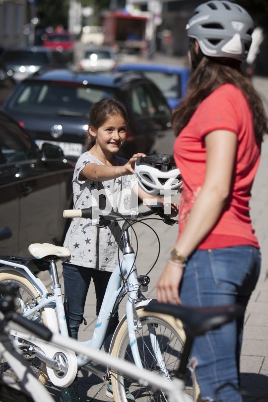 Eine Frau reicht einem Mädchen neben einem Fahrrad einen Helm.