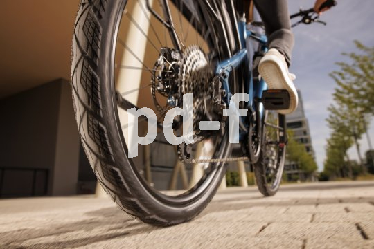 Detailansicht des Hinterreifens eines Fahrrades beim Rollen über eine gepflasterte Oberfläche.