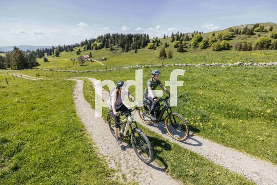 Zwei Frauen fahren einen Weg auf einer Bergwiese entlang.