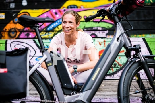 Eine Frau sitzt lächelnd hinter einem abgestellten E-Bike.