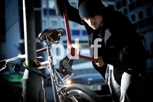 Ein Mann setzt einen Bolzenschneider an einem Bügelschloss an, mit dem ein Fahrrad an einem Metallpfosten gesichert ist.