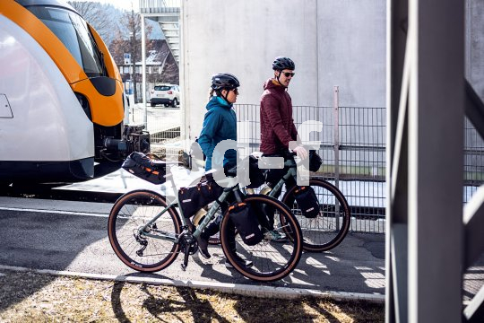Rahmennahe Gepäcklösungen, wie sie für das Bikepacking typisch sind, erleichtern auch das Ein- und Ausladen der Räder aus öffentlichen Verkehrsmitteln. Zwei Personen schieben Fahrräder mit Gepäck daran von einem Zug weg.