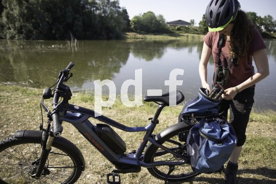 Eine Frau steht neben einem E-Bike und packt etwas in oder aus einer von zwei Packtaschen am Gepäckträger.