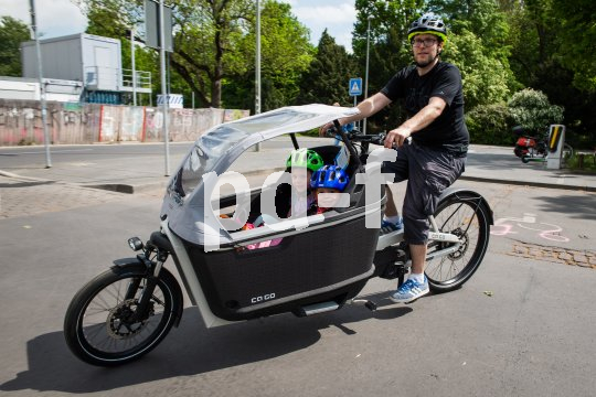 Ein Mann fährt ein Lastenrad mit zwei Kindern und Regenverdeck.