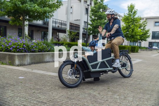 Ein Mann fährt auf einem Lastenrad mit zwei Kindern an Bord durch ein Wohngebiet.