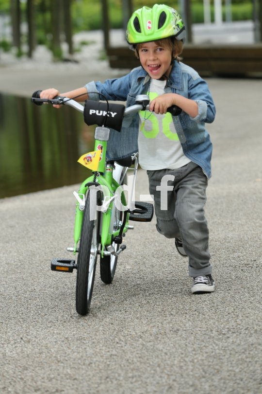 Ein Kind mit grünem Helm schiebt ein grünes Fahrrad.