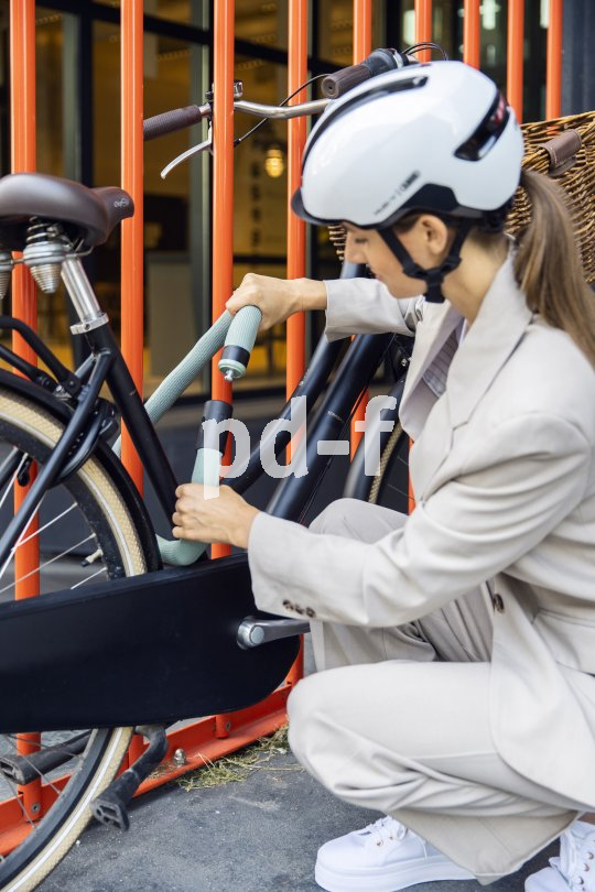 Eine Frau schließt ihr Fahrrad an einem roten Metallzaun an.