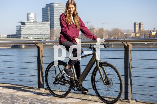 Eine Frau sitzt auf einem E-Bike und hält sich am Geländer eines Flussufers fest.