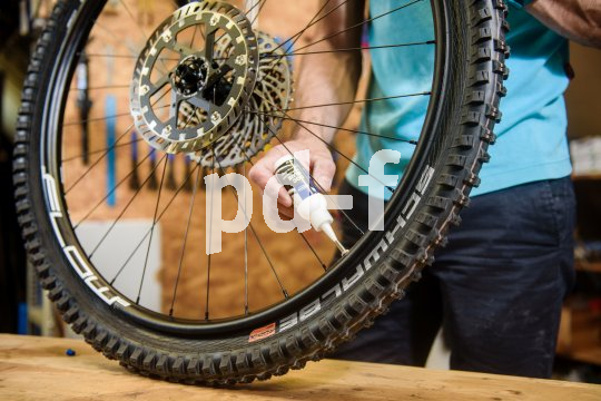 Eine Person hält das Hinterrad eines Mountainbikes auf einer Werkbank und setzt eine kleine Plastikflasche mit Dichtflüssigkeit an das Ventil an.