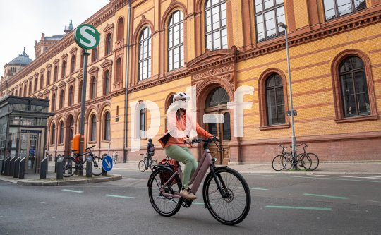 Eine Frau fährt auf einem E-Bike vor einem Gebäude entlang, vor dem ein rundes Schild mit einem weißen S auf grünem Grund steht.