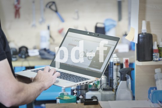 Die Bildunterschrift wird in Bälde eingefügt. Sie können uns aber gern auch per E-Mail oder Telefon kontaktieren, wir helfen gerne weiter. Eine Person hält in einer Werkstatt einen Laptop vor sich, auf dessen Bildschirm ein E-Bike zu sehen ist.