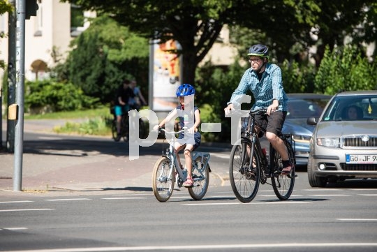 Ein Kind und ein Mann fahren nebeneinander auf Fahrrädern auf einer Straße.