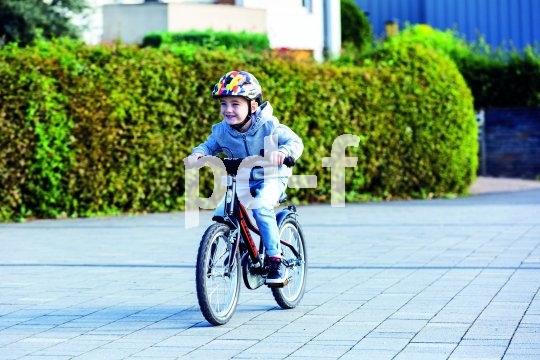Ein Kind mit buntem Helm fährt mit einem Fahrrad über einen Platz.
