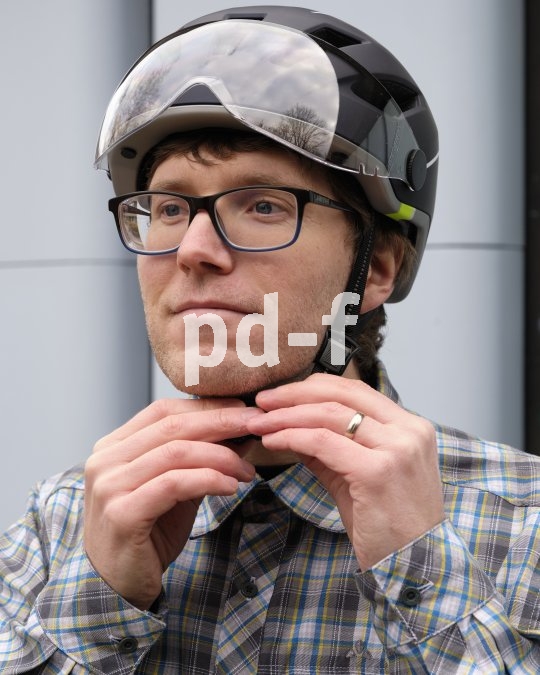 Ein Mann mit Fahrradhelm bedient den Verschluss des Helmriemens unterm Kinn mit beiden Händen.