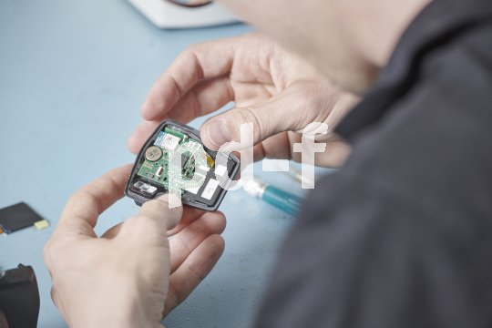 Blick über die Schulter einer Person, die ein offenes elektronisches Bauteil in den Händen hält.