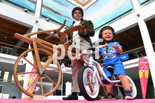 Ein Kind mit einem Laufrad vor einem Mann mit einem historischen Laufrad aus Holz.